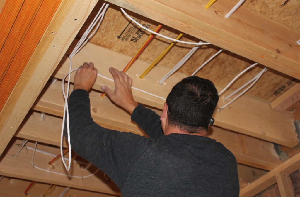 Installer running low voltage cable through open ceiling joists during construction